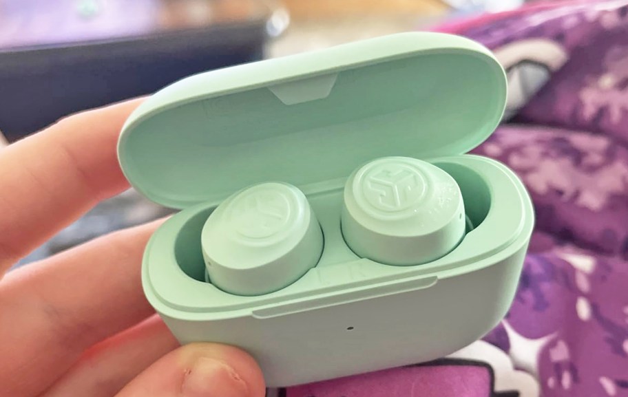 hand holding a pair of mint green earbuds in their charging case