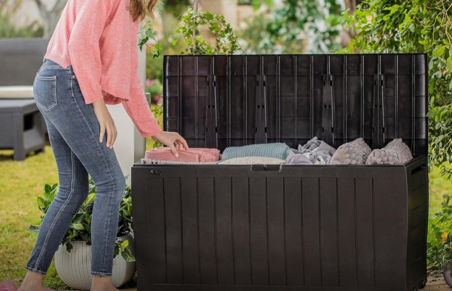A woman putting pillows into a Keter storage box.