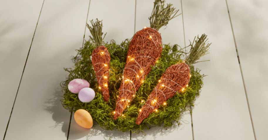 Three light up carrots inside of a basket with greenery