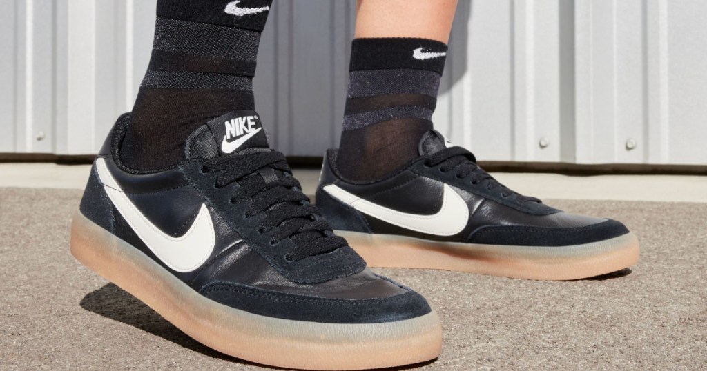 Person wearing black and white Nike shoes with black socks and standing outside