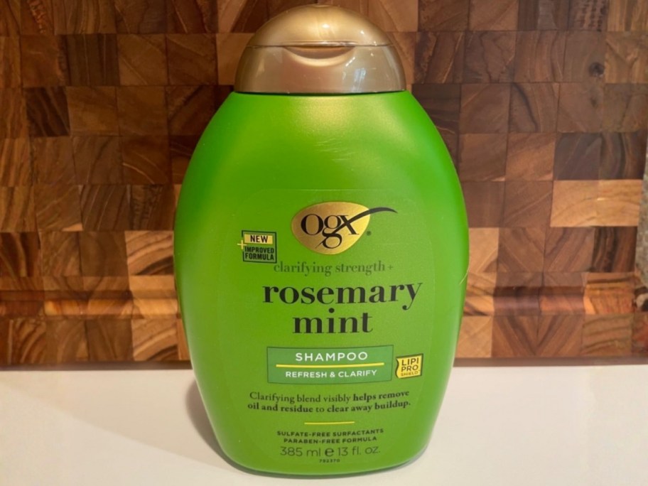 bottle of ogx rosemary mint shampoo with checkered wood background