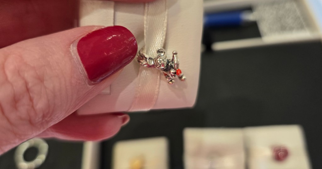 Woman with red nails, holding up Pandora, Disney charm