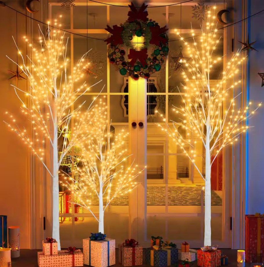 3 lighted birch trees with presents around them