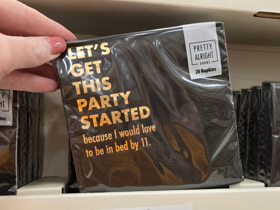 hand holding a pack of napkins that says "Let's Get This Party Started because I would love to be in bed by 11"
