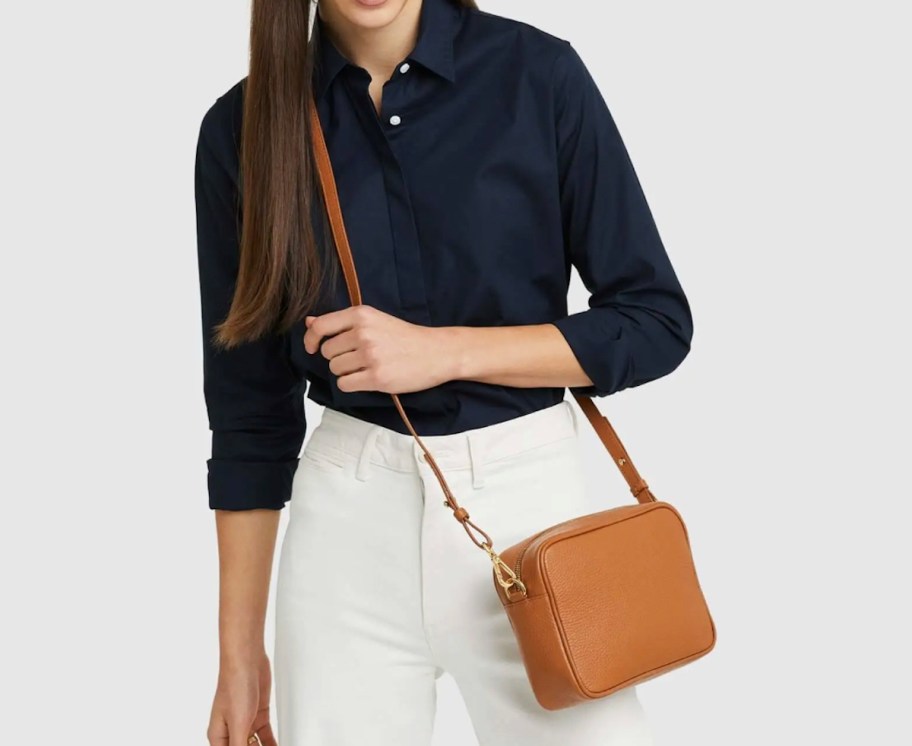 woman holding camel colored crossbody purse on body