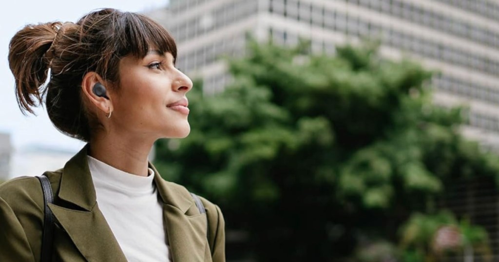 Woman wearing black Samsung earbuds and walking outside in front of office building