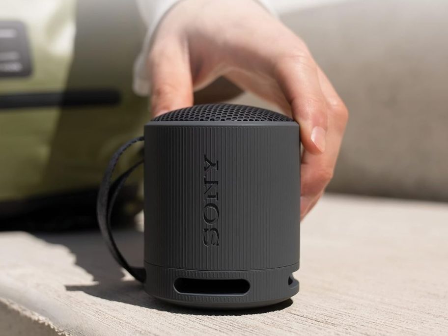 A person touching a small black speaker