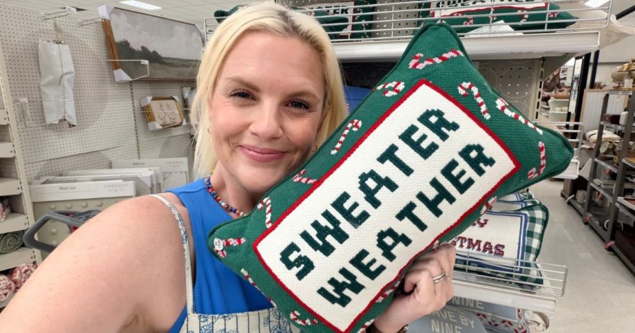 Stefanie holding Sweater Weather Cross Stitch Pillow in store