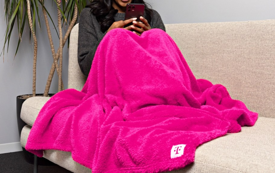 woman on a couch under a bright pink blanket