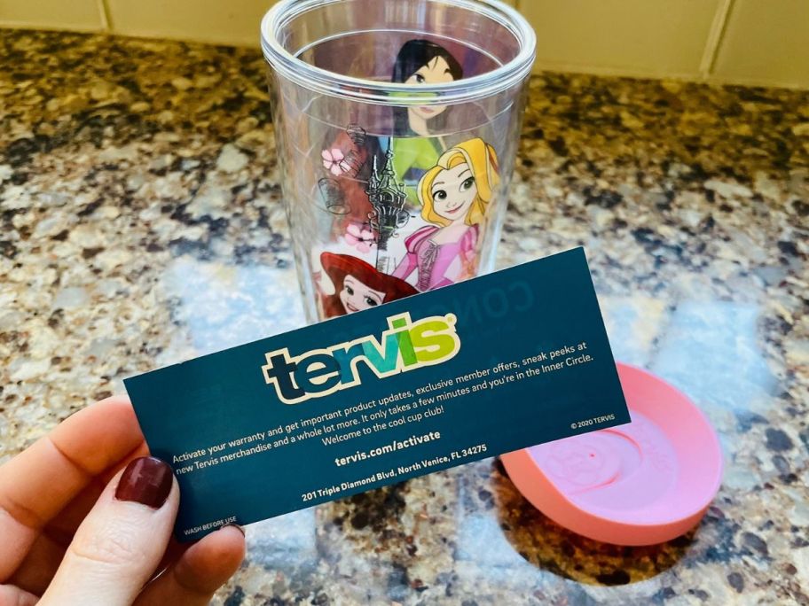 Hand holding a card with Tervis Warranty info on it in front of an empty tervis cup