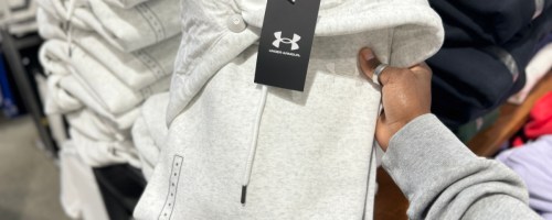 Woman taking gray under Armour hoodie off of store shelf