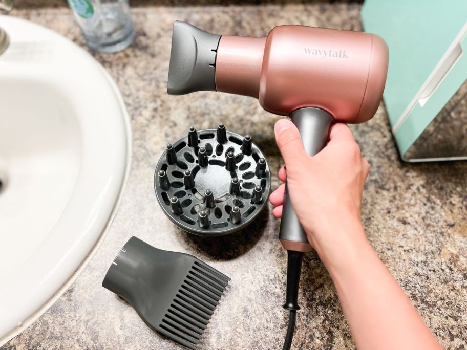 hnad holding wavytalk hair dryer in her hand with accessories on the table