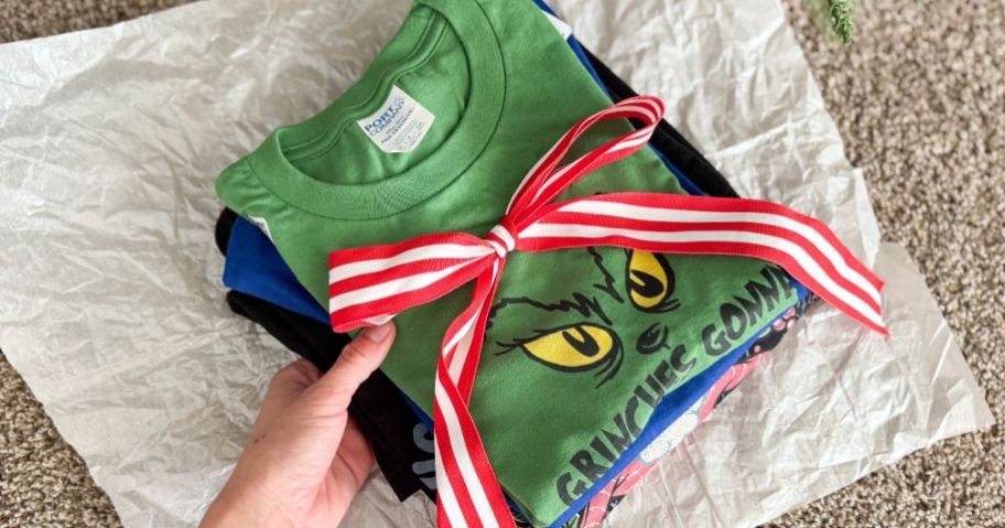 A Stack of folded graphic tees from woot wrapped with a red and white bow