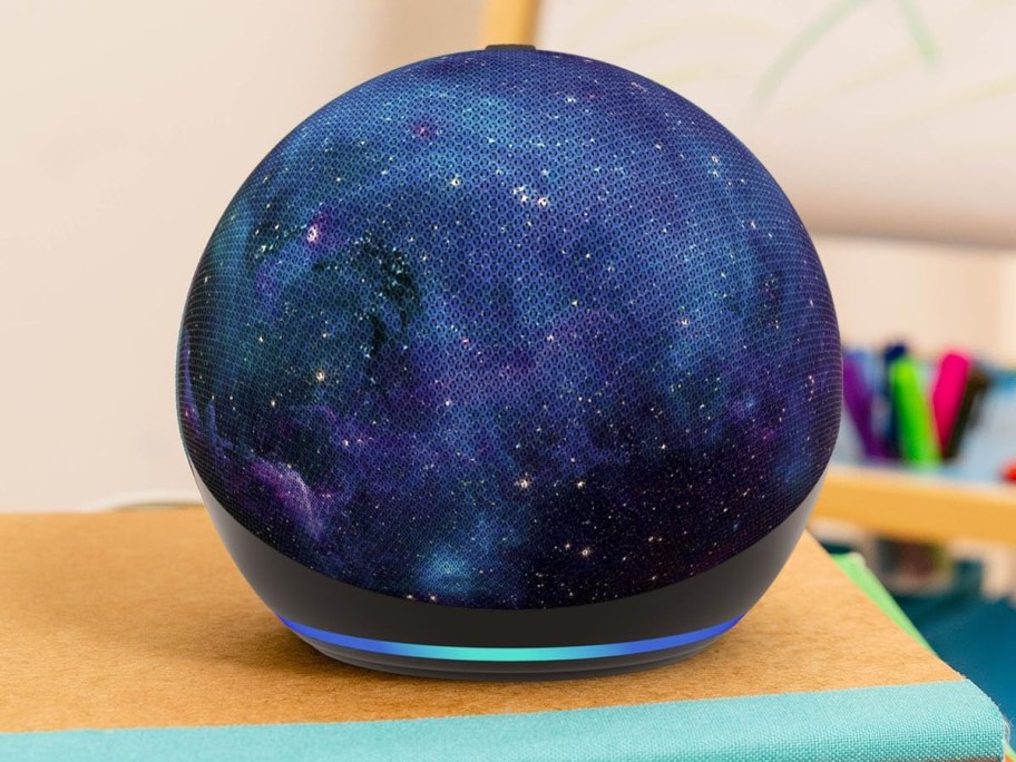 An Amazon Echo Dot smart speaker featuring a blue and purple stardust galaxy pattern sitting on a surface.