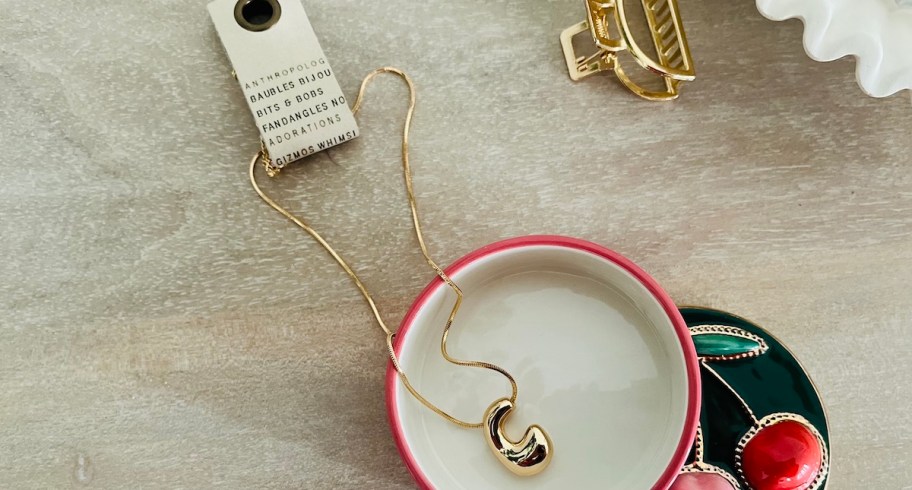 gold c necklace in dish on wood table