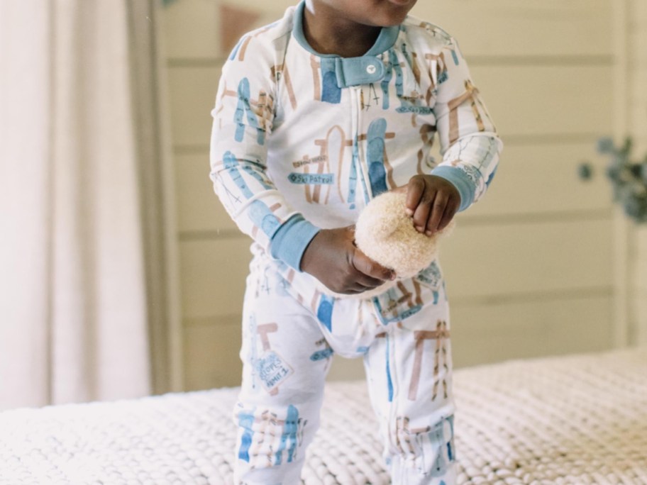 A child wearing white Burt's Bees Baby footed pajamas with a blue ski pattern, holding a small stuffed animal.