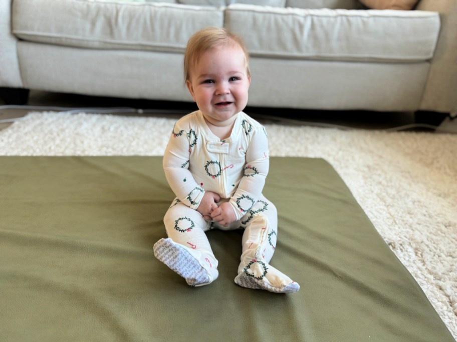baby sitting on the floor wearing christmas wreath PJs
