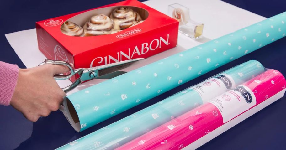 person cutting wrapping paper next to Cinnabon box