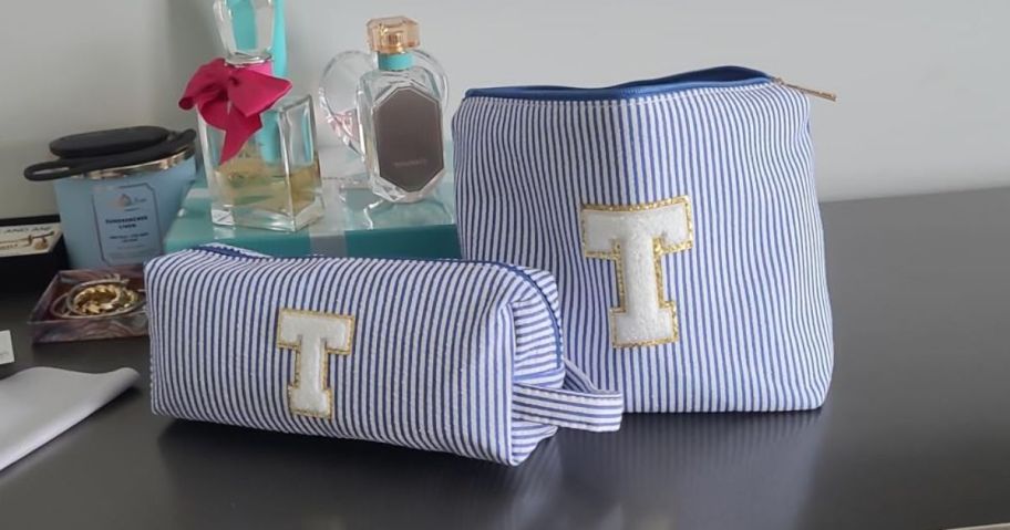 two blue striped cosmetic bags with a T on them on dresser