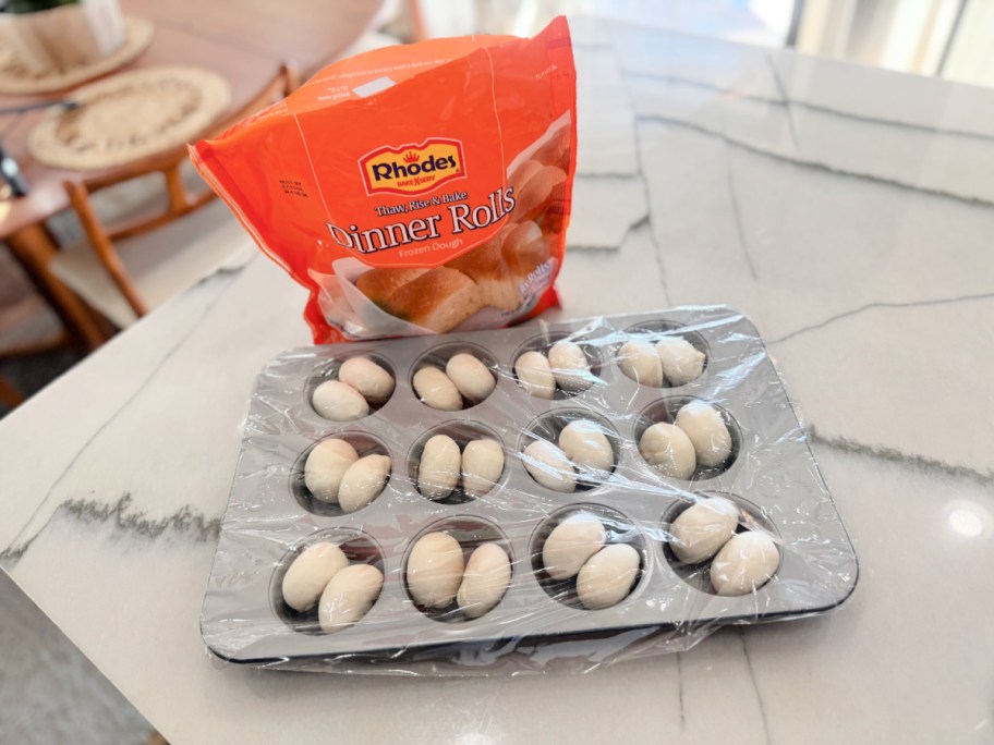 dinner rolls inside a muffin pan with plastic wrap on top 