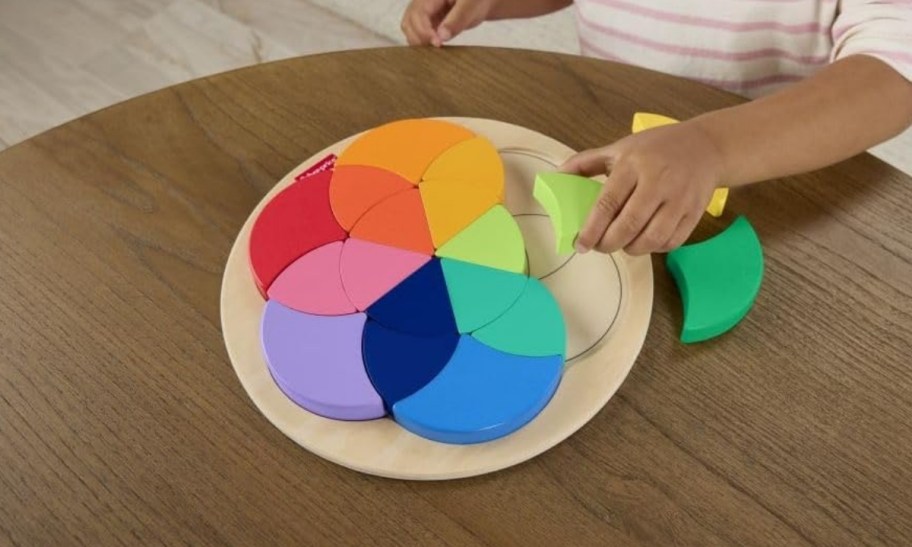 a toddlers hand assembling a color wheel puzzle 