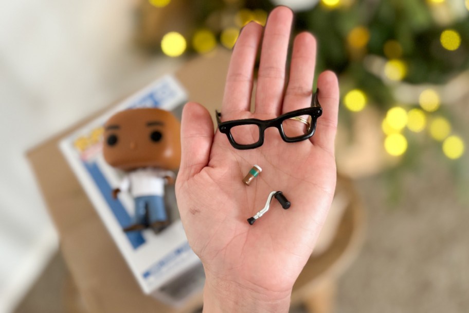 hand holding mini coffee mug, cane, and glasses