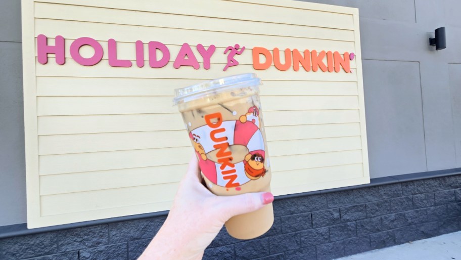 hand holding up a dunkin drink in front of a dunkin holiday sign