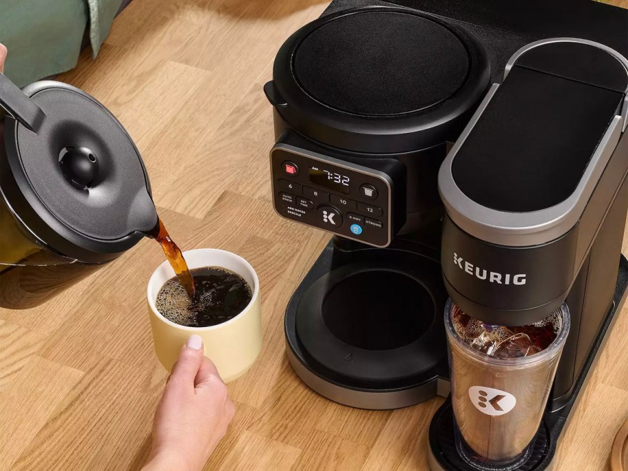 black keurig maker on counter with person pouring coffee into white mug 