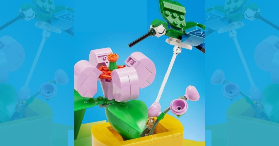 A colorful LEGO scene featuring a green and blue hummingbird hovering near a pink flower.