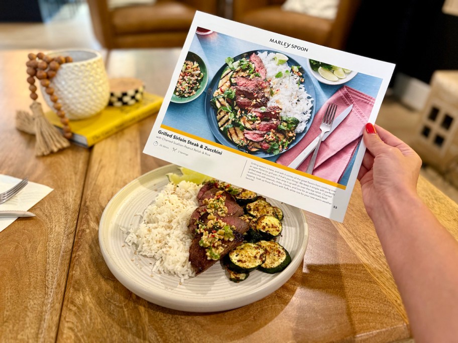 hand holding recipe paper with plate of matching food on table