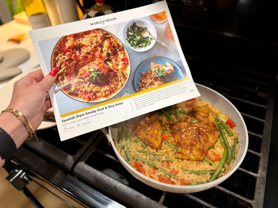 hand holding a marley spoon recipe card over the dish cooking on the stove