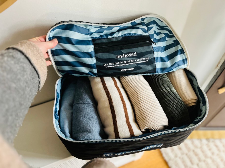 hand holding open nuuly fabric delivery box filled with clothes