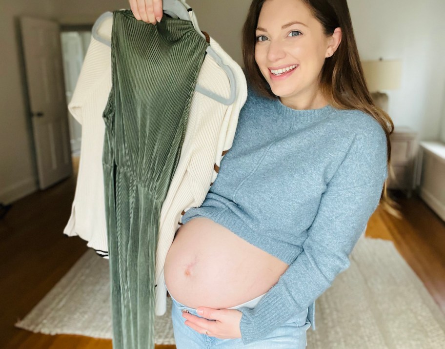 woman holding up clothes on hanger holding pregnant belly