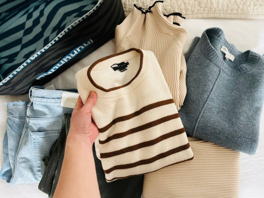hand holding stripe sweater on pile of clothes