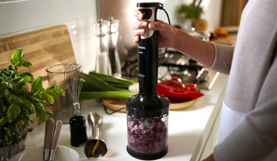 a woman using a philips promix handblender to chop onions