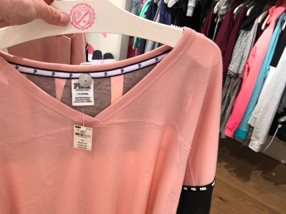 hand holding a hanger with a pink t-shirt on it