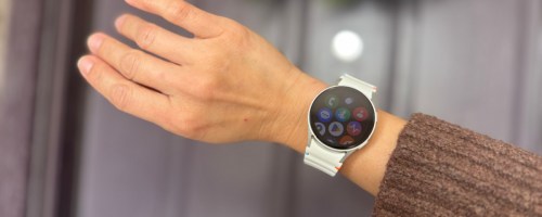 samsung galaxy watch7 on a wrist held in front of a door with a wreath