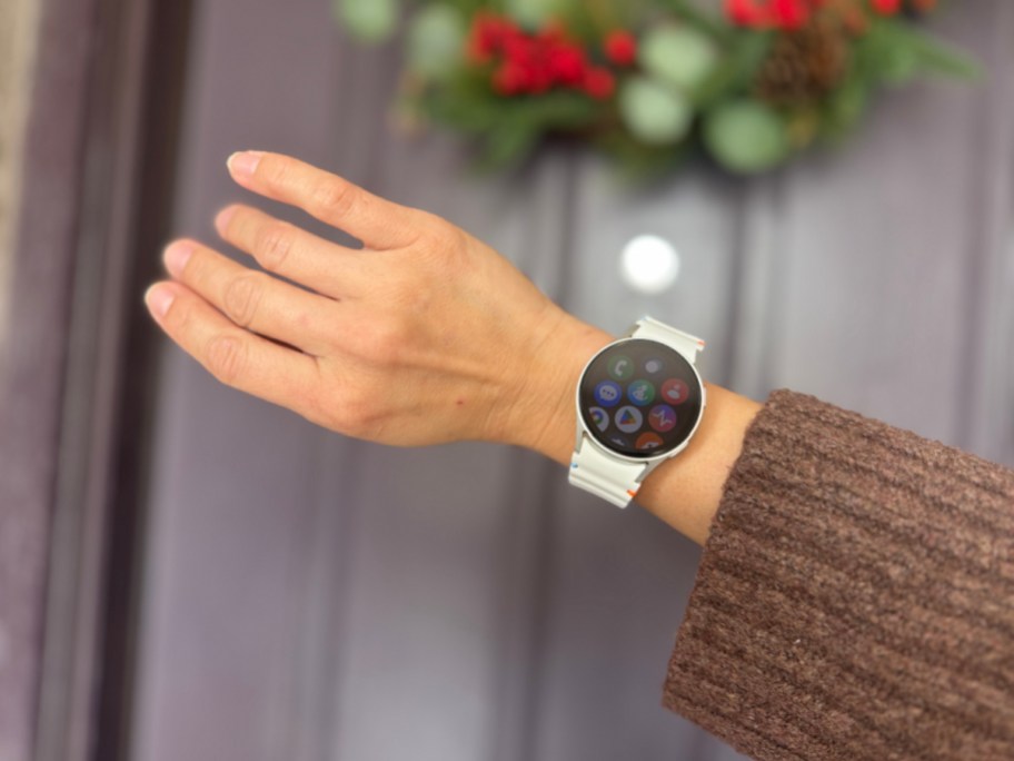 samsung galaxy watch7 on a wrist held in front of a door with a wreath