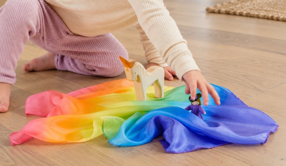 toddler playing with animals on rainbow playsilk