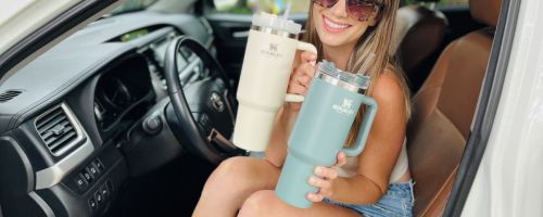 A woman holding two Stanley tumblers in a car.