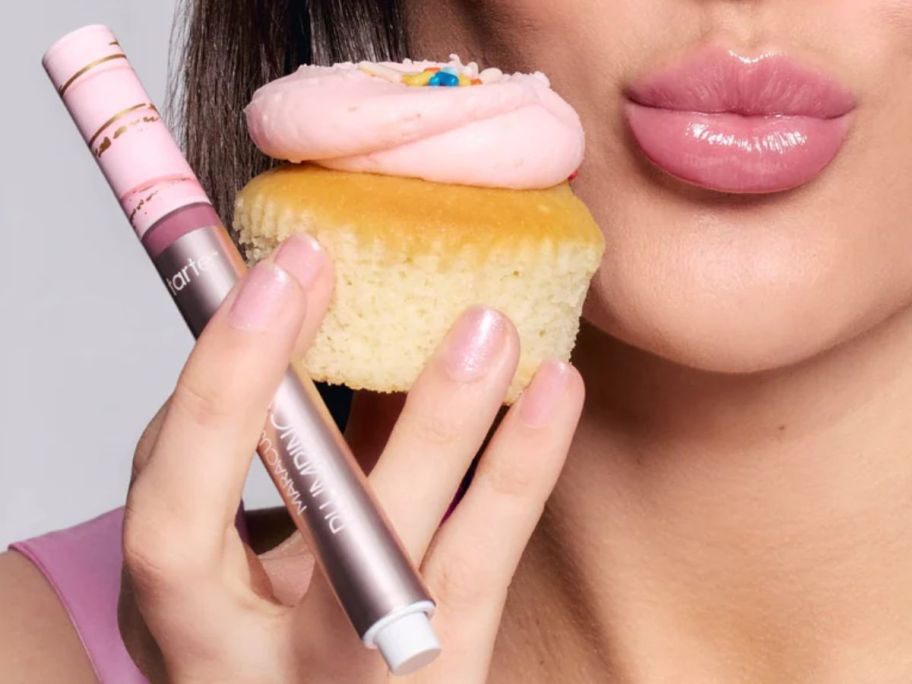 Woman holding a cupcake and a tarte maracuja juicy lip next to her lips