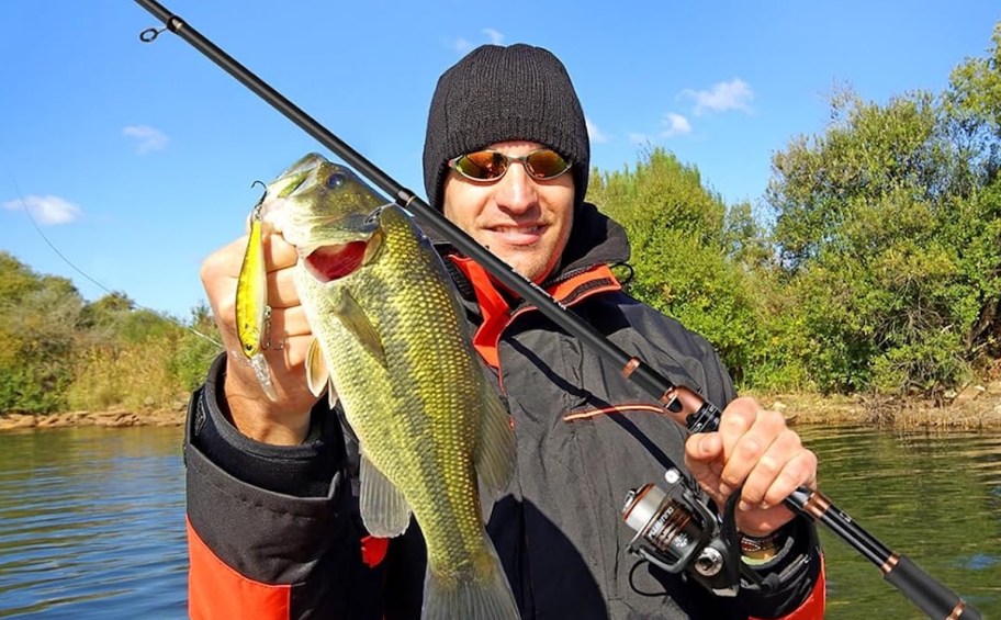man holding fish and rod on boat in lake