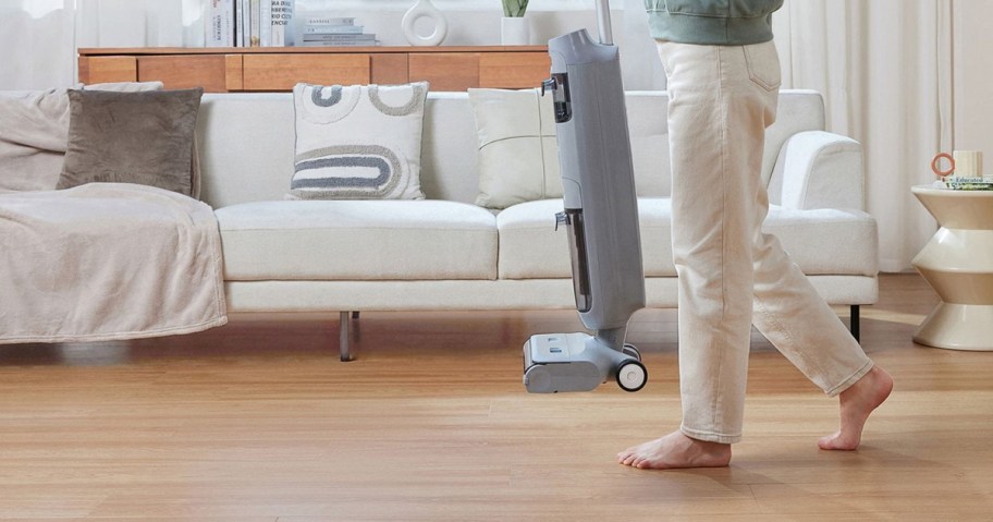person carrying a tineco vacuum through a living room
