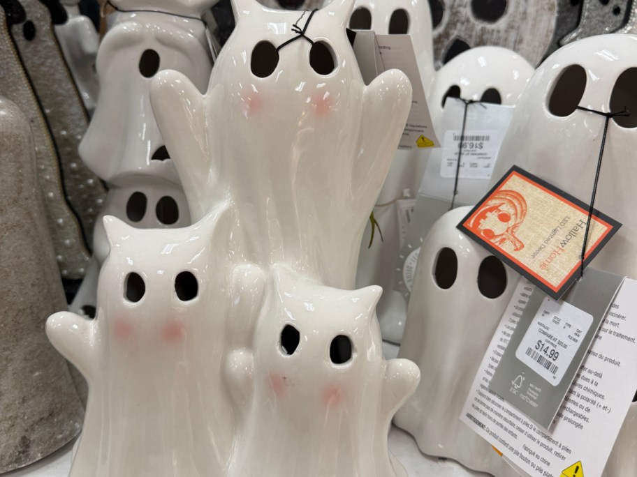 A cluster of white ceramic ghost figurines with pink cheeks and cutout eyes on a store shelf.