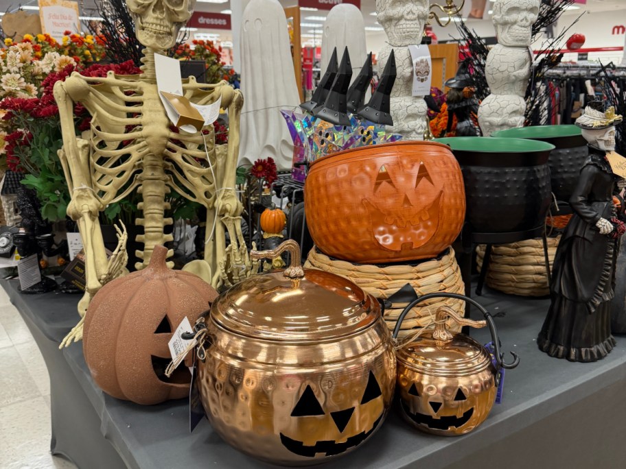 A display of Halloween decor items, featuring metallic copper pumpkin containers, a skeleton, and spooky decorations on a store table.