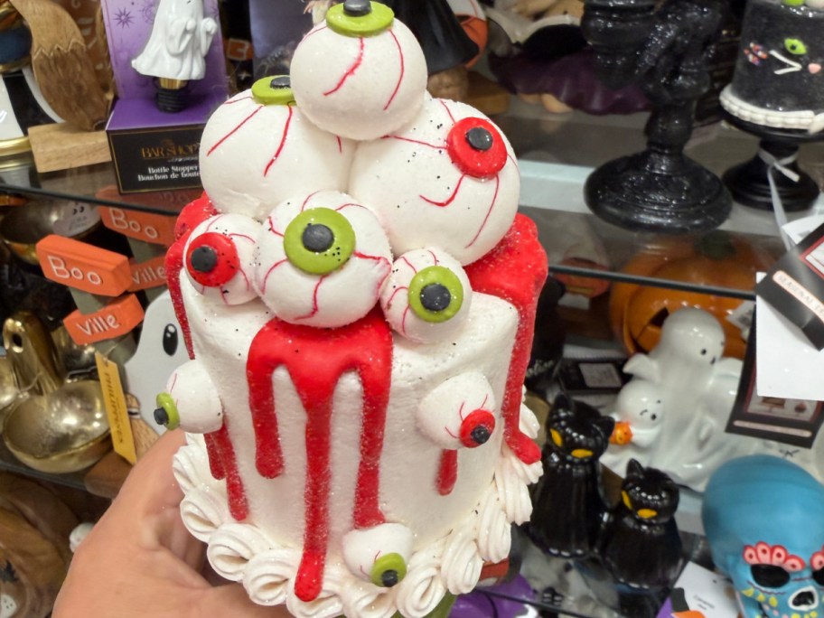A decorative Halloween cake figurine topped with stacked white and green eyeballs and dripping red icing.