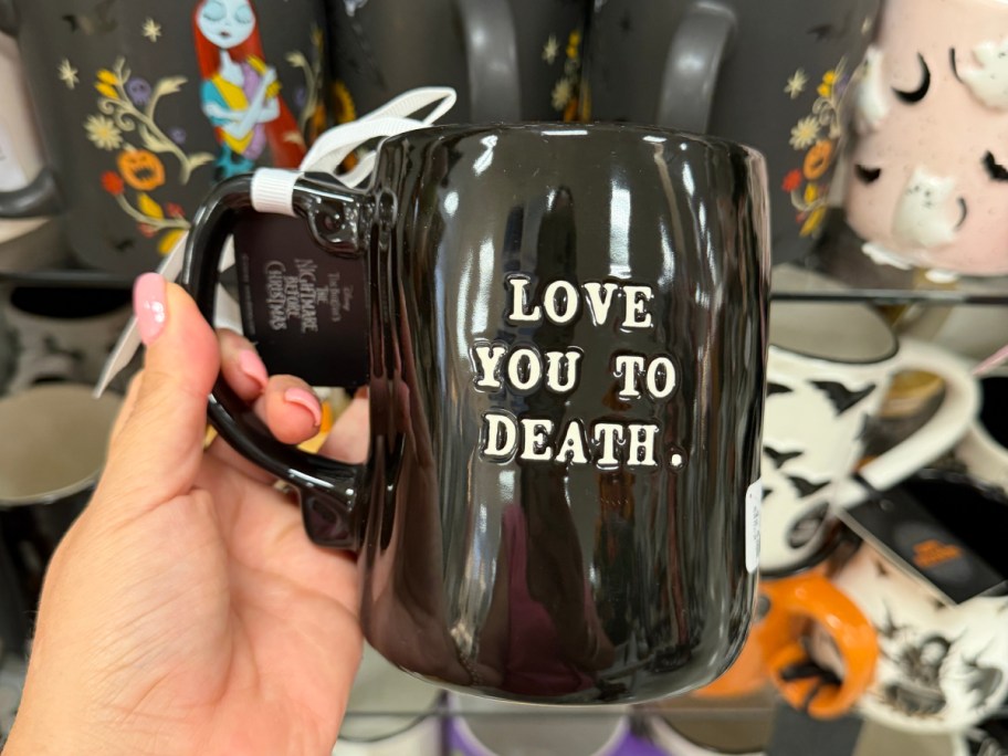 A glossy black ceramic mug with raised white text that reads "LOVE YOU TO DEATH."