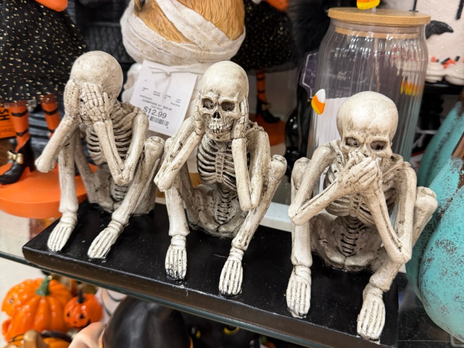 A set of three skeleton figurines depicting "see no evil, hear no evil, speak no evil" sitting on a black base.