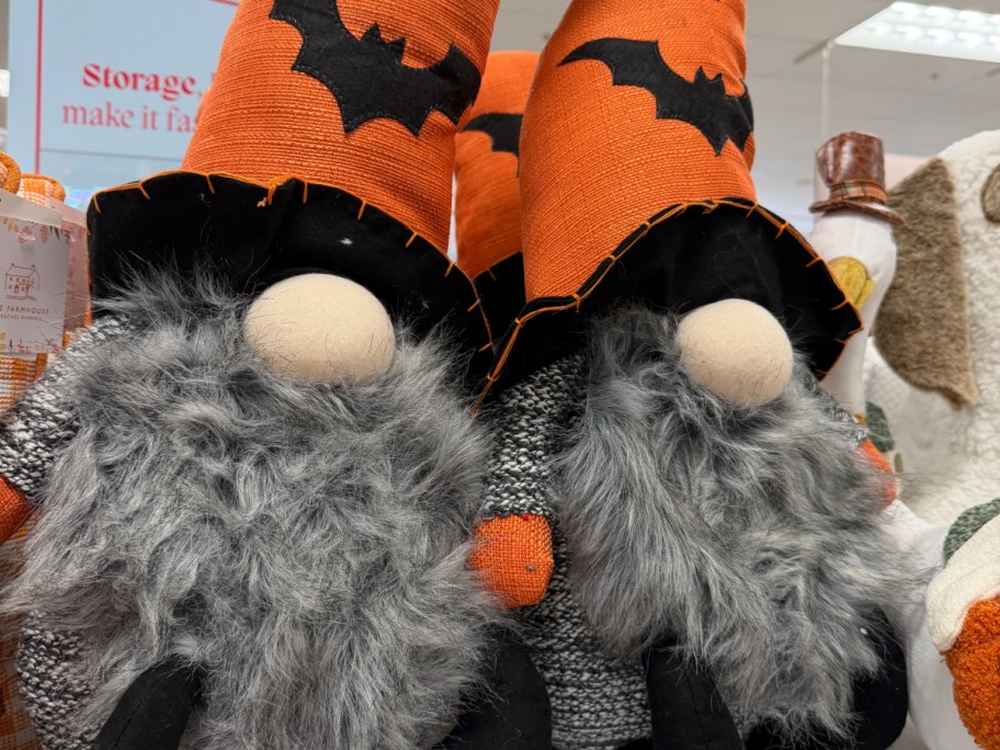 Two Halloween gnome plush toys with tall orange and black bat-patterned hats and fluffy grey beards.