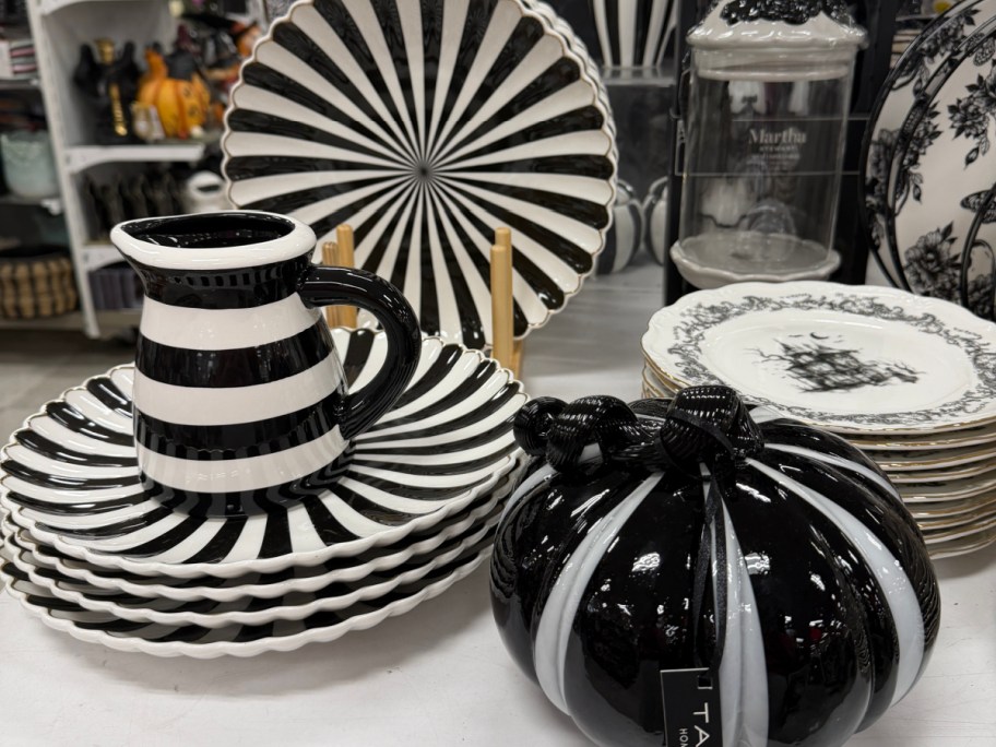 A display of black and white tableware, featuring striped plates, a matching pitcher, and a black-and-white pumpkin figurine.